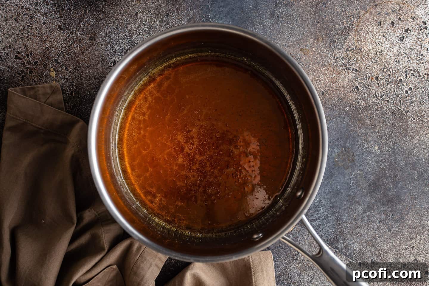 The sugar syrup has transformed into a beautiful, deep amber-brown caramelized sugar in a stainless steel pot.