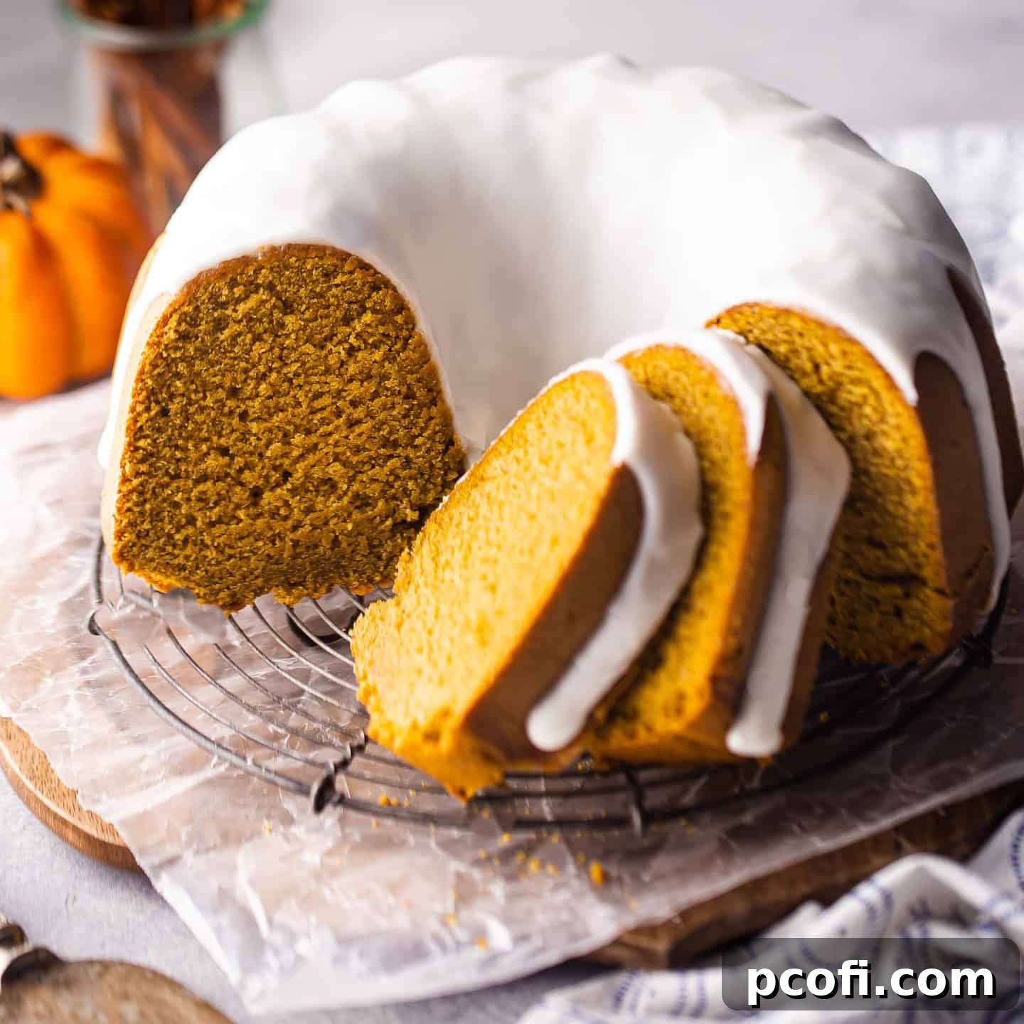 Pumpkin bundt cake with cream cheese glaze sliced and presented on a wire rack.