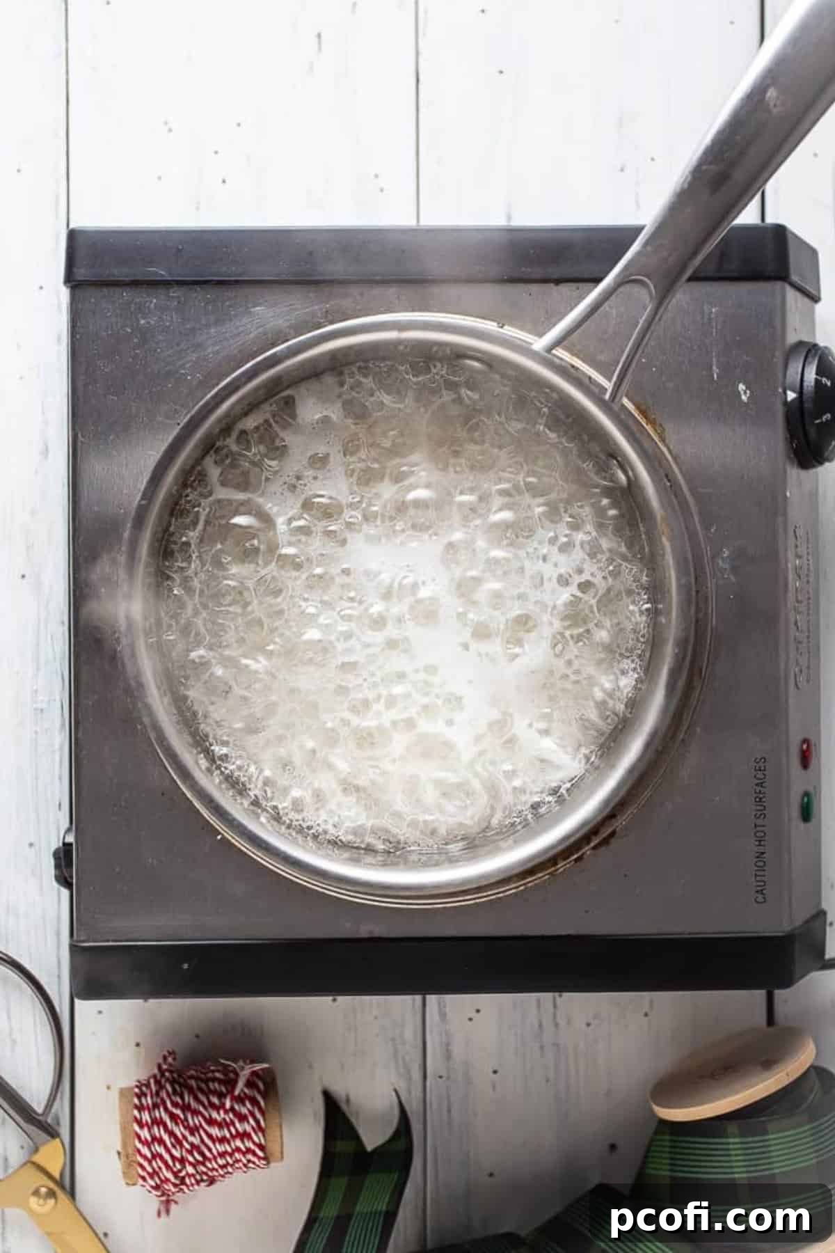 Boiling sugar syrup in a small saucepan, with a candy thermometer showing temperature.