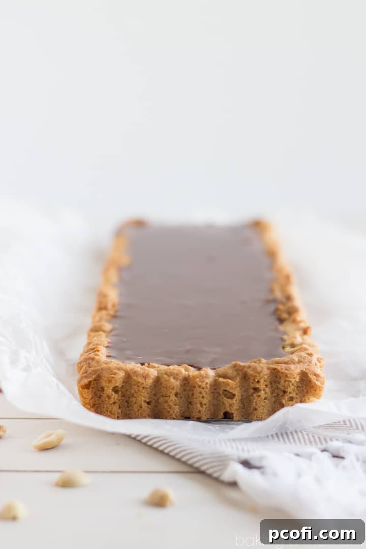 A finished Snickers Blondie Tart, sliced to reveal layers of peanut butter blondie, peanuts, salted caramel, and milk chocolate ganache.