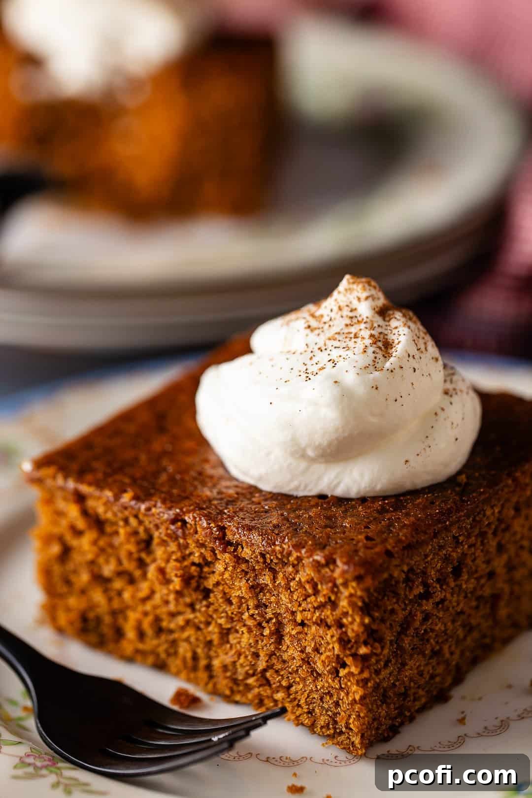 A perfectly sliced piece of old-fashioned gingerbread cake, topped with a dollop of whipped cream, invitingly presented on a delicate plate, hinting at its soft, moist texture and rich, spicy aroma.