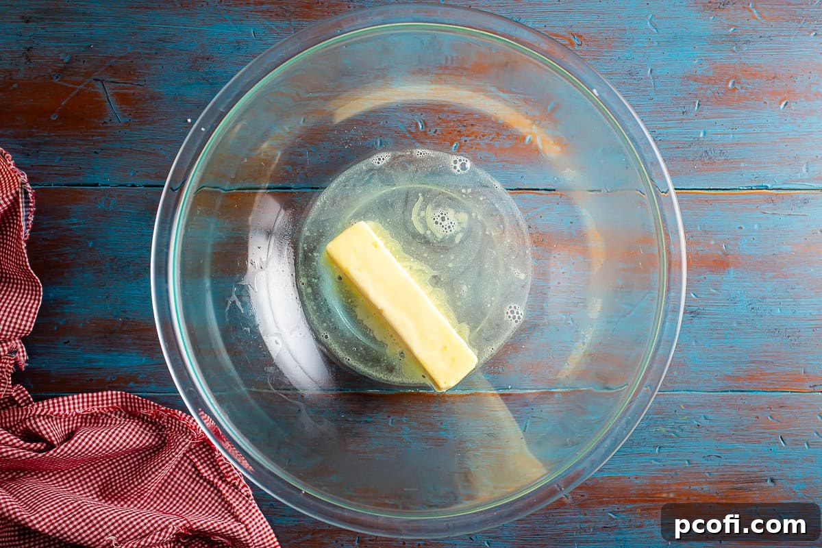 Hot water being poured over softened butter in a large glass mixing bowl, initiating the melting process for the gingerbread cake base.