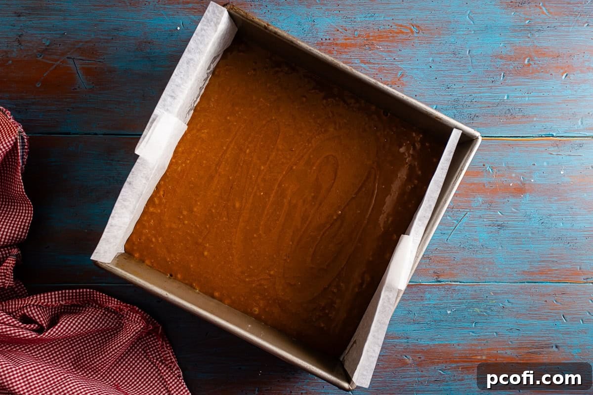 The unbaked gingerbread cake batter evenly distributed in the prepared square baking pan, smooth on top and ready to be placed into the oven.