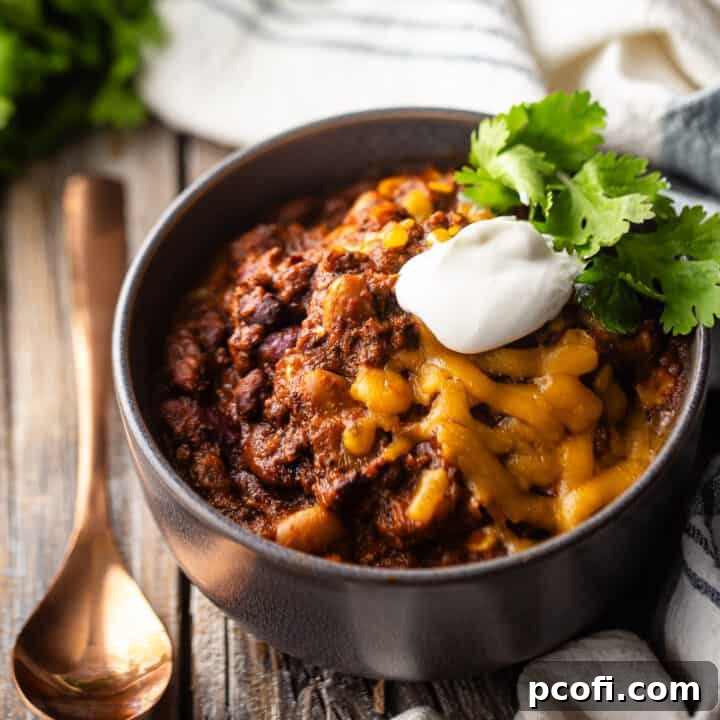 Best chili con carne recipe ever, served in a gray ceramic bowl with a copper spoon, garnished with fresh herbs.