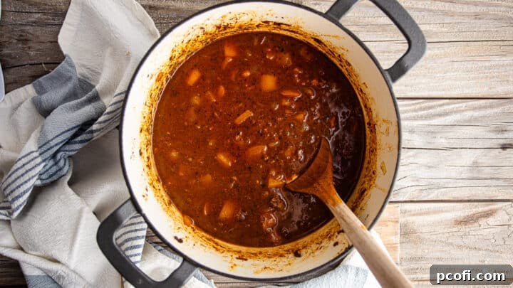 Adding beef stock to the beef chili recipe, deglazing the pot to capture rich flavors.