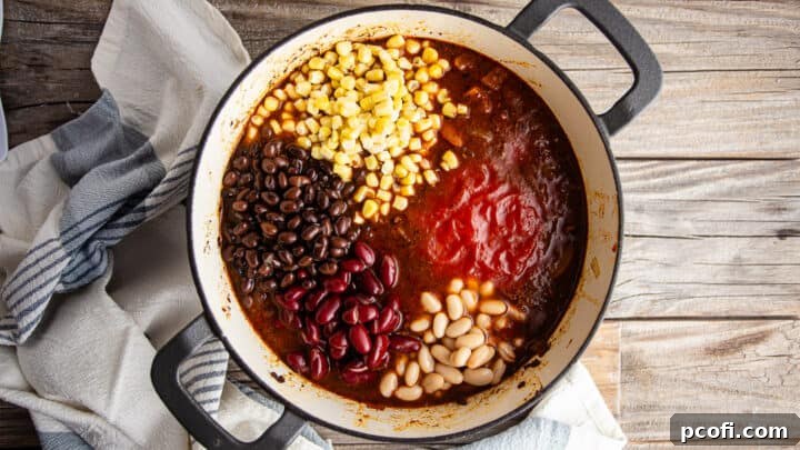 Adding crushed tomatoes, beans, and corn to the crockpot chili recipe for simmering.
