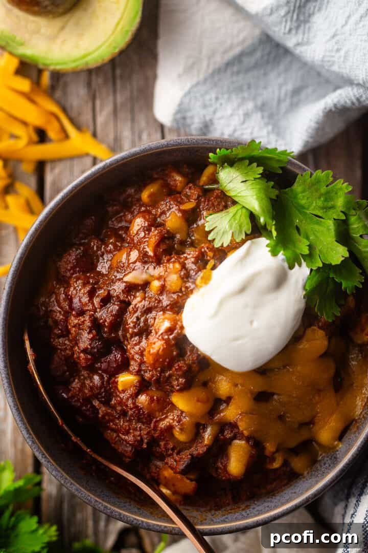Beef chili recipe, prepared, cooked, and topped generously with cheese, sour cream, and fresh cilantro in a bowl.