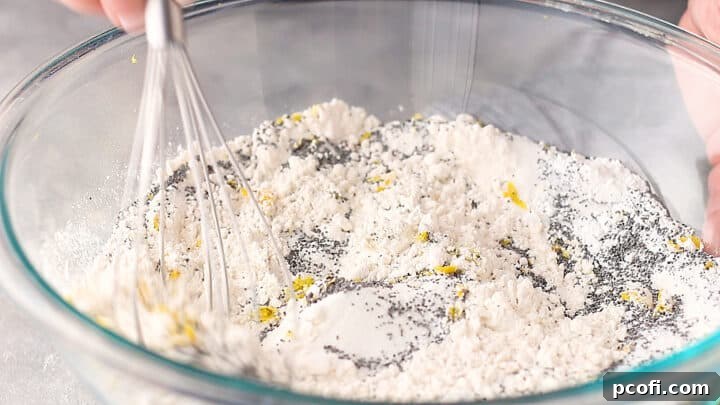Stirring dry ingredients for lemon poppy seed muffins together with a whisk in a large mixing bowl.