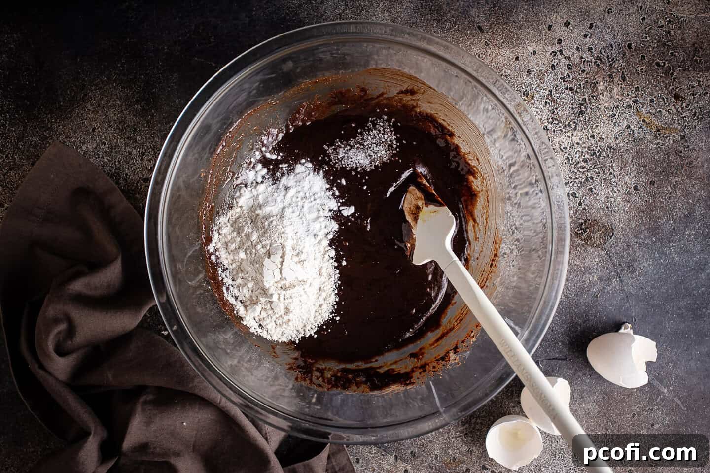 Adding dry ingredients (flour, baking powder, salt) to the rich, glossy brownie batter.