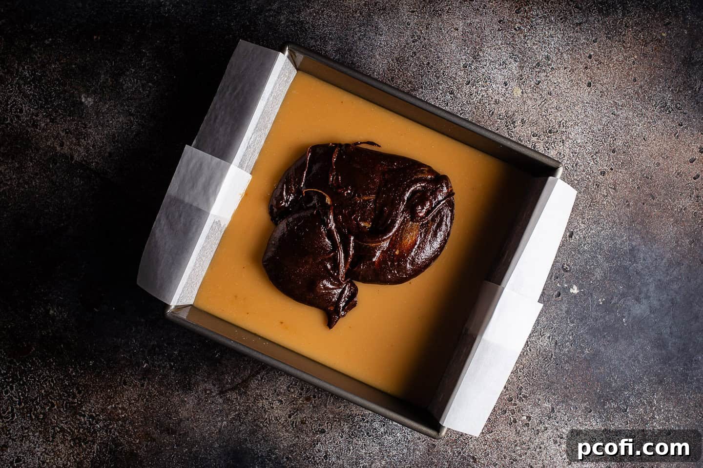 Carefully layering brownie batter over the cooled and set salted caramel layer in the baking pan.