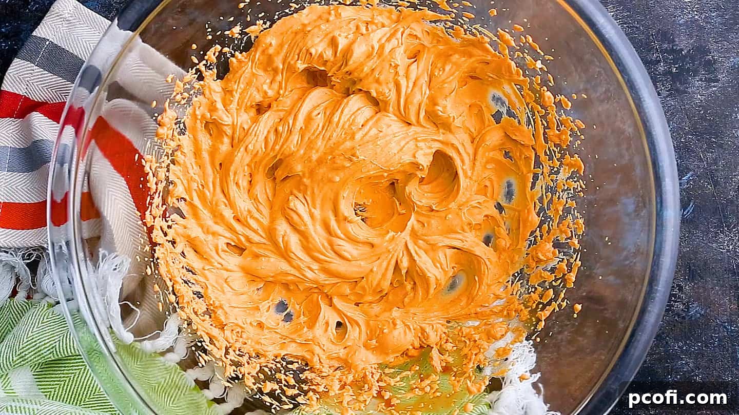 Cream cheese, sour cream, and buffalo sauce blended together in a large glass mixing bowl for the creamy base of the dip.