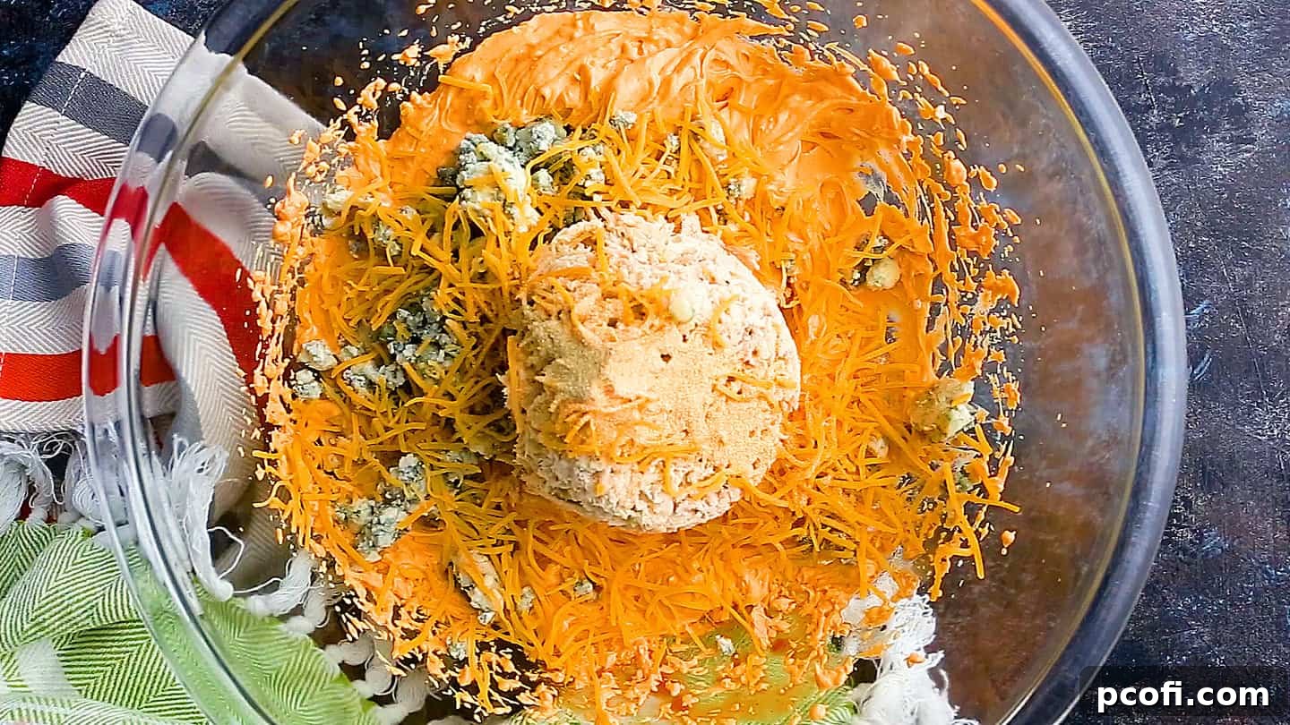 Adding shredded chicken, blue cheese, and cheddar cheese to the buffalo chicken dip base.