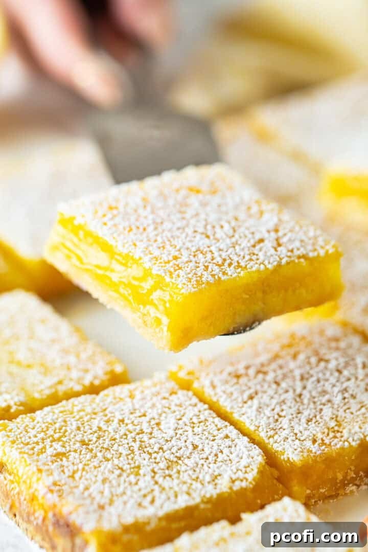 Lifting freshly baked lemon bars from the cutting board with a spatula.