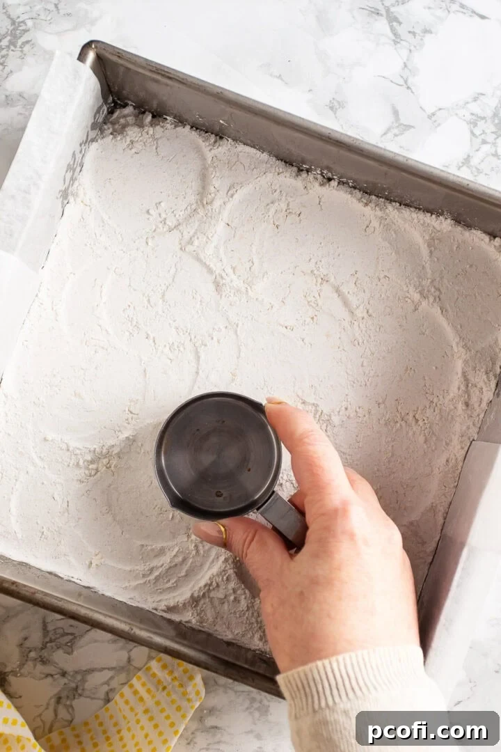 Pressing crust mixture into a square pan with the bottom of a measuring cup.