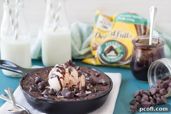 A top-down view of the warm chocolate mint skillet brownie, showcasing its fudgy interior and melted mint chocolate chips. It's garnished with a dusting of powdered sugar and fresh mint leaves, ready to be served.
