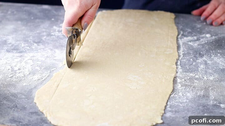 Trimming uneven edges off of croissant dough with a pizza cutter.