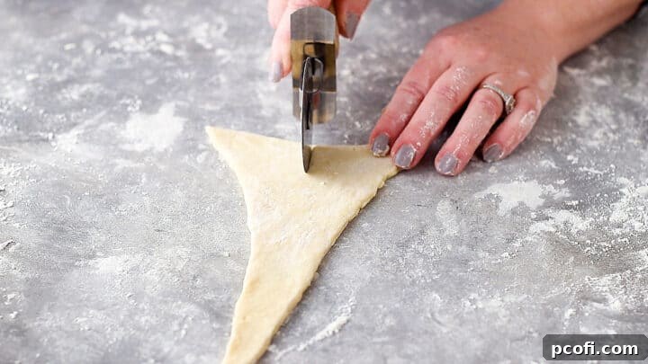 Cutting a notch into the wide end of a triangle of croissant dough.
