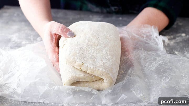 Homemade croissant dough, rolled and folded several times and being wrapped in plastic wrap.