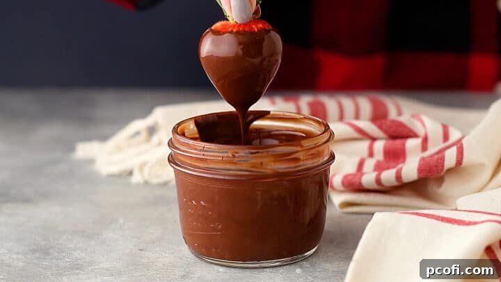 Dipping a fresh strawberry into smooth melted chocolate and allowing excess to drip away.