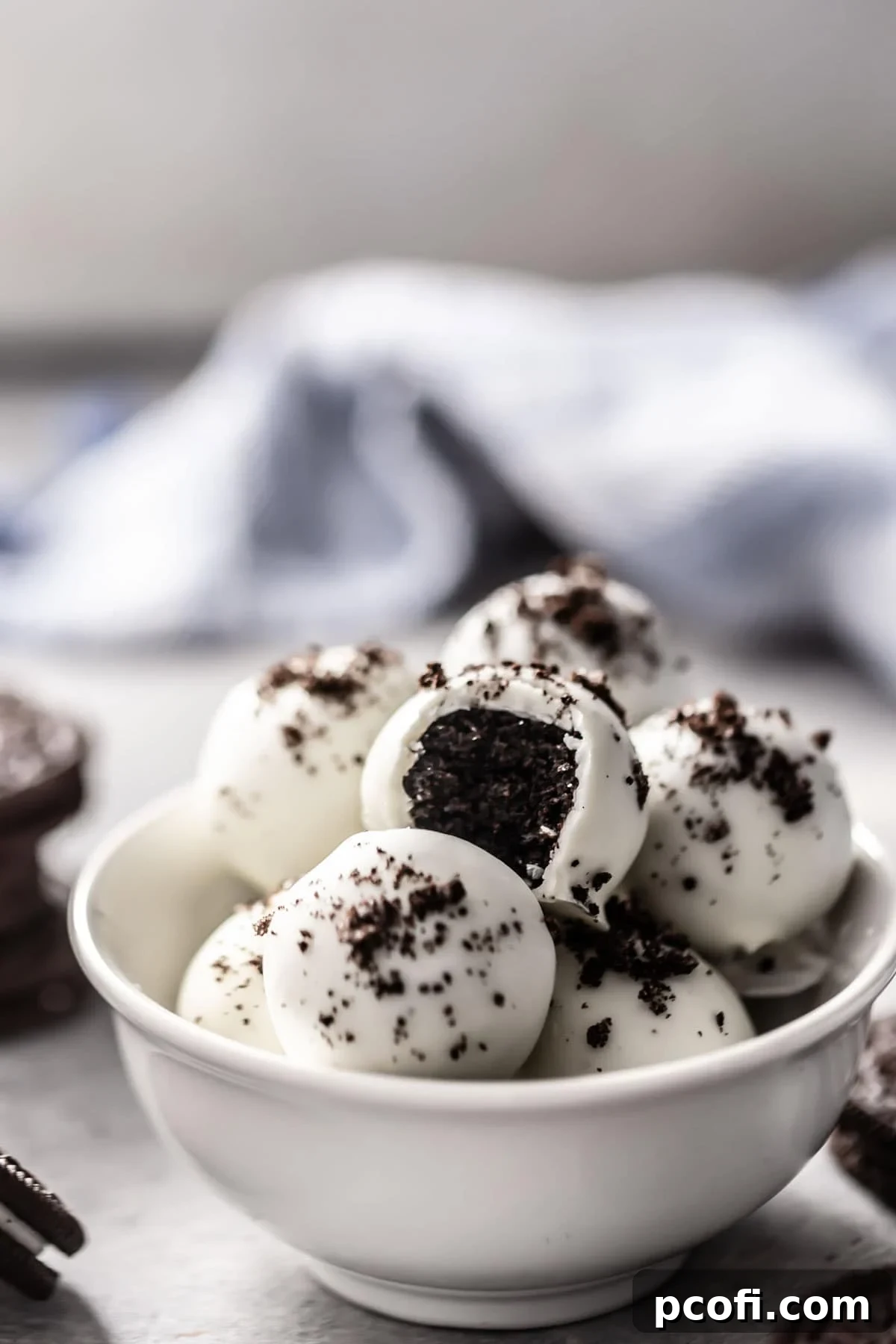 Delicious Oreo truffle balls, freshly made and coated in white chocolate, with one bitten to show the creamy center, garnished with crushed Oreo crumbs.