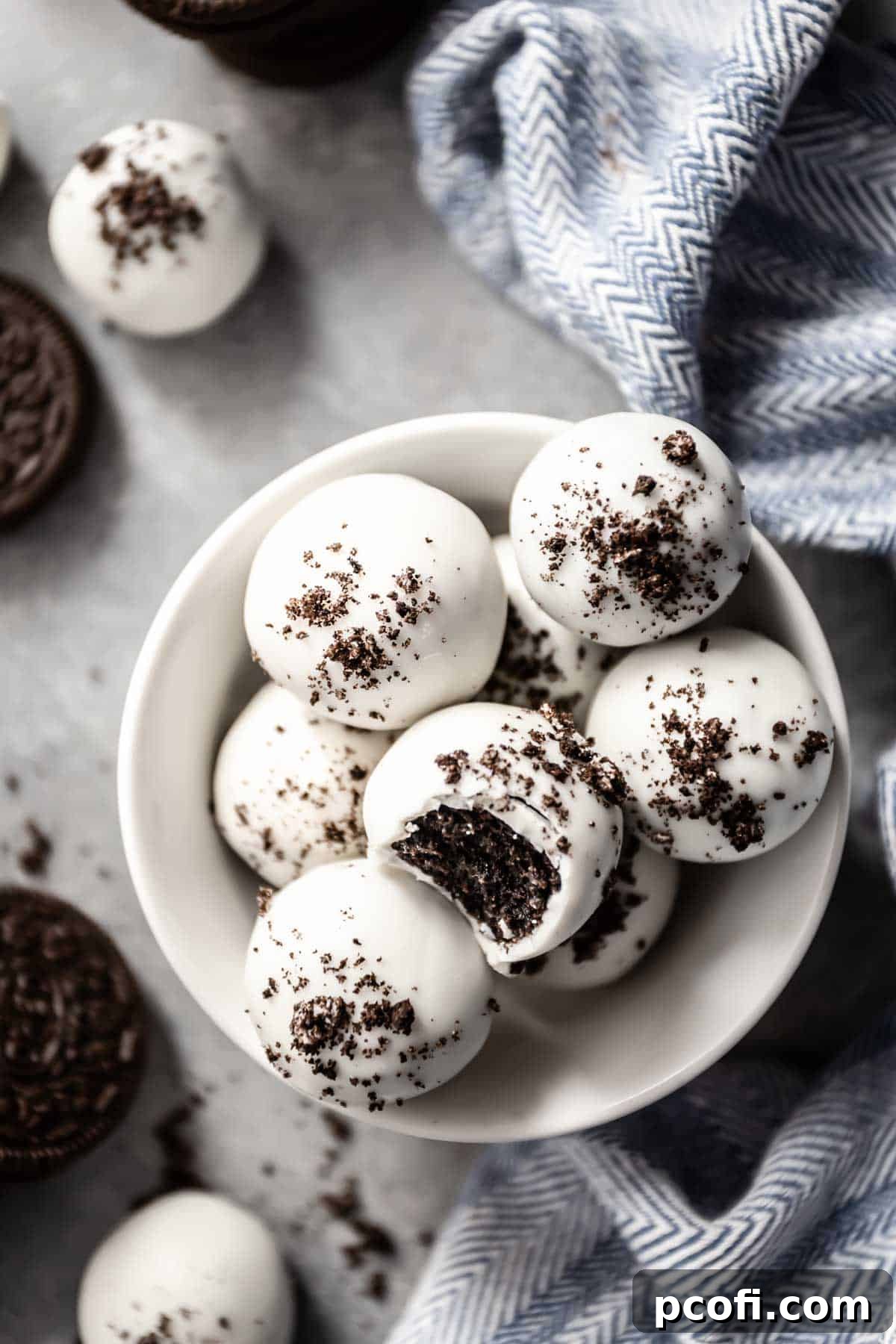 An inviting overhead view of freshly coated Oreo balls resting in a pristine white bowl, beautifully adorned with white chocolate and a dusting of fine Oreo crumbs.