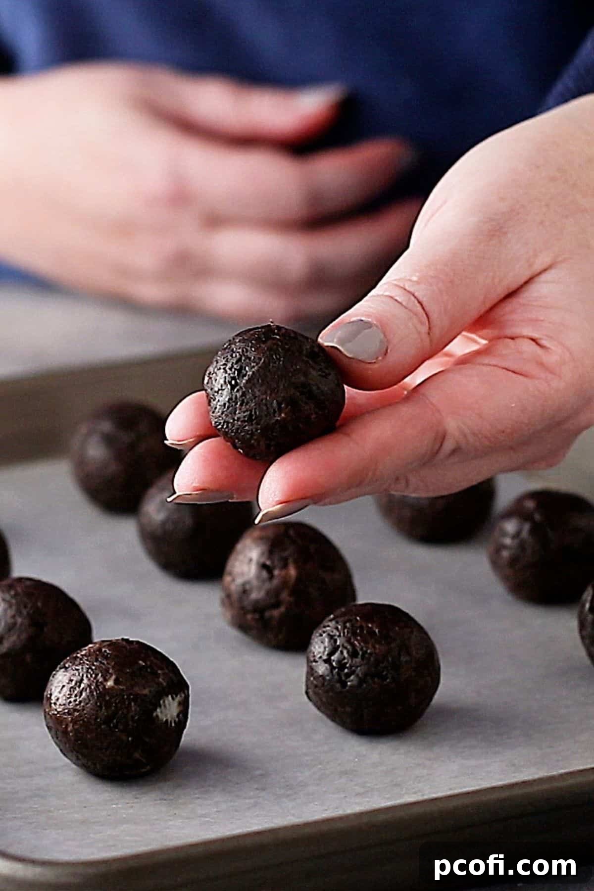 Hands gently rolling the sticky Oreo and cream cheese mixture into perfectly smooth, uniform balls before chilling.