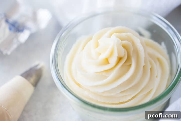 Close up of a glass bowl filled with cream cheese frosting, piped in a swirl pattern.