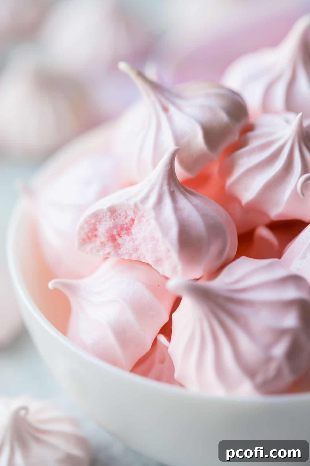 Close-up image of a baked meringue cookie with a bite taken out of it, showing the light and airy interior, highlighting its delicate structure.