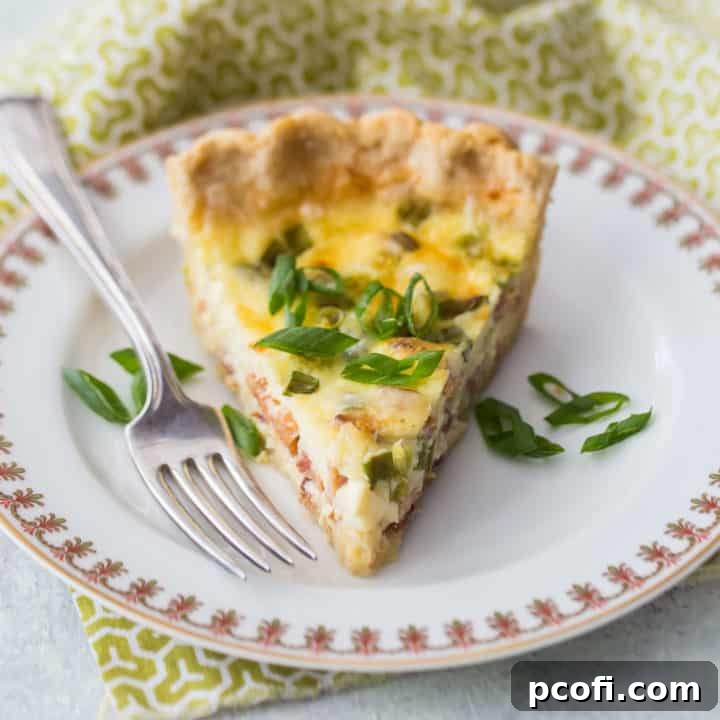 A slice of quiche Lorraine on a china plate with a green printed napkin, highlighting its silky texture and flaky crust.