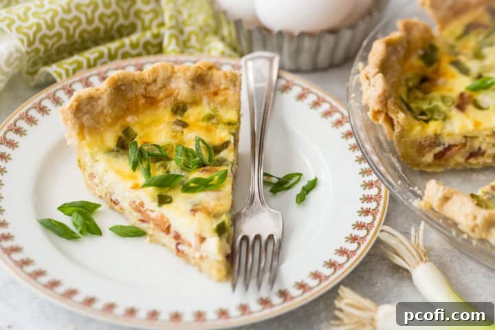A single slice of quiche Lorraine resting on a china plate with a silver fork beside it, garnished with a sprinkle of fresh sliced scallions.