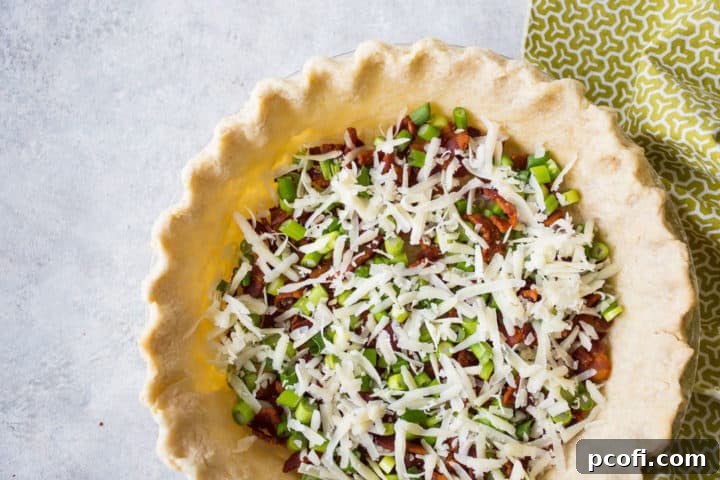 Cooked bacon, sliced scallions, and shredded Gruyere cheese scattered evenly in the bottom of a blind-baked pie crust.