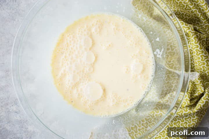 A large mixing bowl filled with the smooth, pale yellow quiche custard mixture, ready to be poured into the pie crust.