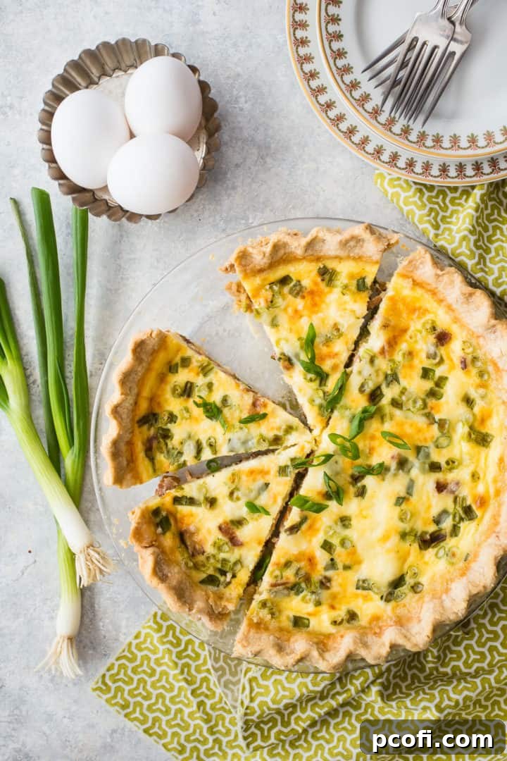 Overhead image of a beautifully baked quiche Lorraine, garnished with fresh scallions, ready to be served.