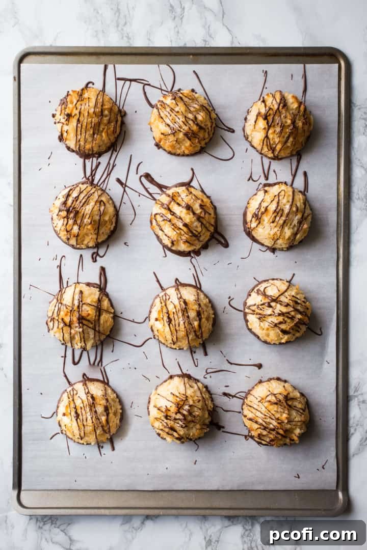 Overhead image of coconut macaroons dipped in dark chocolate on a parchment-lined baking sheet.