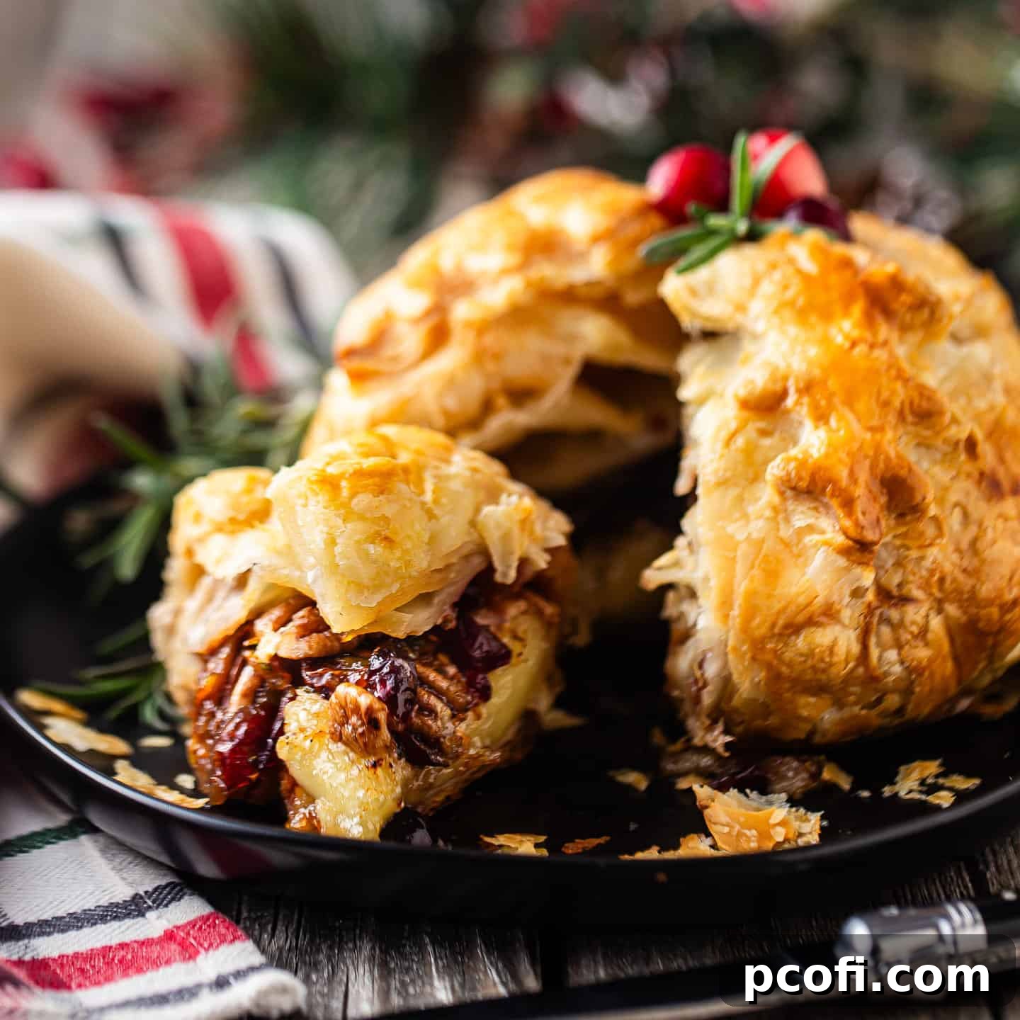 Baked Brie in puff pastry with a wedge cut out, showcasing the melted cheese and cranberry-pecan filling.