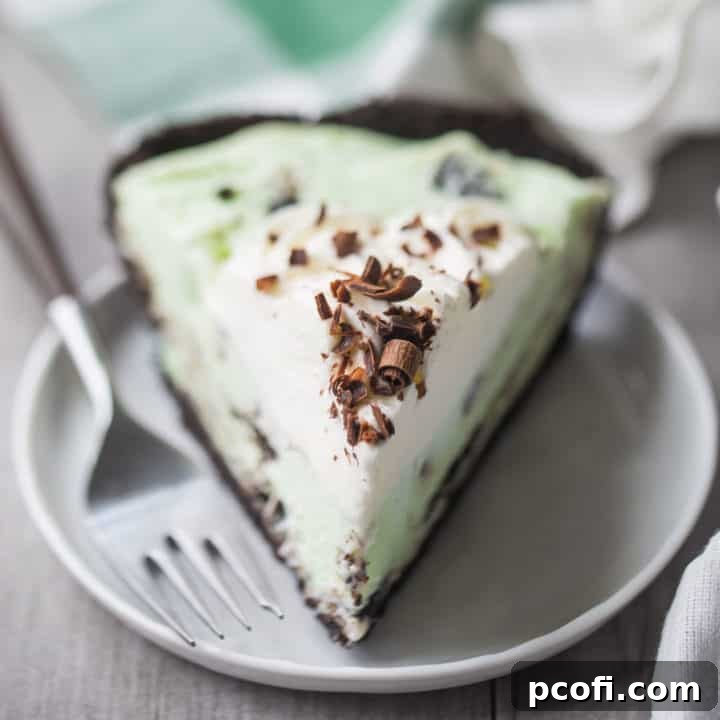 A slice of grasshopper pie with whipped cream and chocolate shavings, on a white plate with a green plaid napkin in the background.
