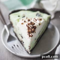 A slice of grasshopper pie with whipped cream and chocolate shavings, on a white plate with a green plaid napkin in the background.