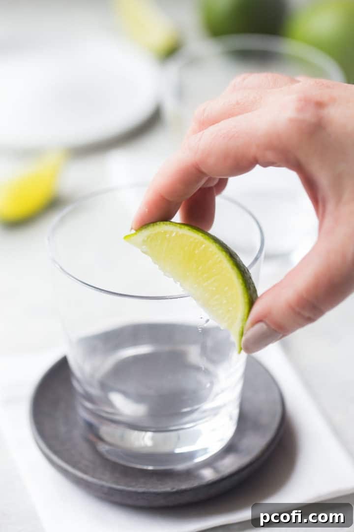 A lime wedge being run along the rim of a rocks glass, preparing it for salting.