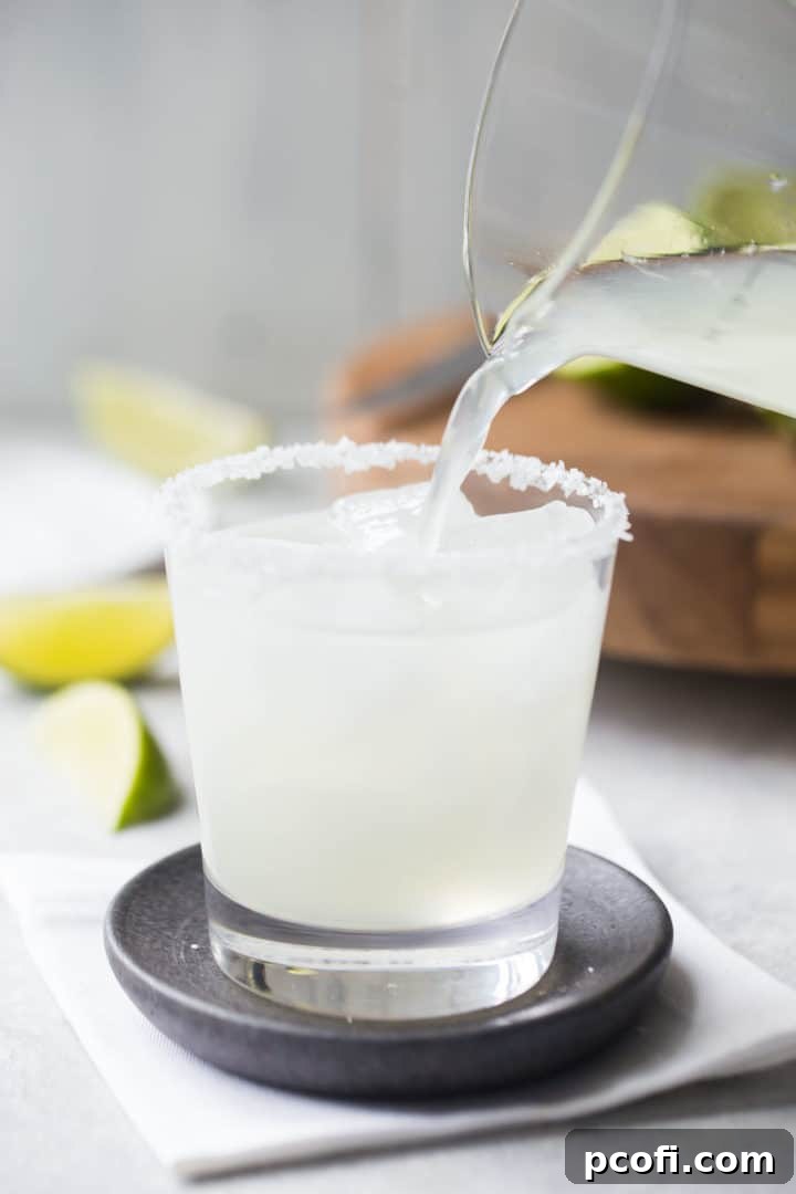 Pouring a freshly mixed margarita cocktail over ice into a rocks glass with a salted rim, ready for enjoyment.