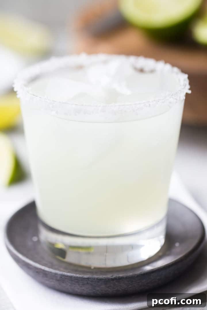 A close-up of a single perfect margarita cocktail, garnished with a lime, in a rocks glass with a salted rim.