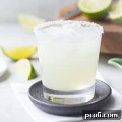 Margarita on the rocks with a salted rim, in a rocks glass with limes in the background.