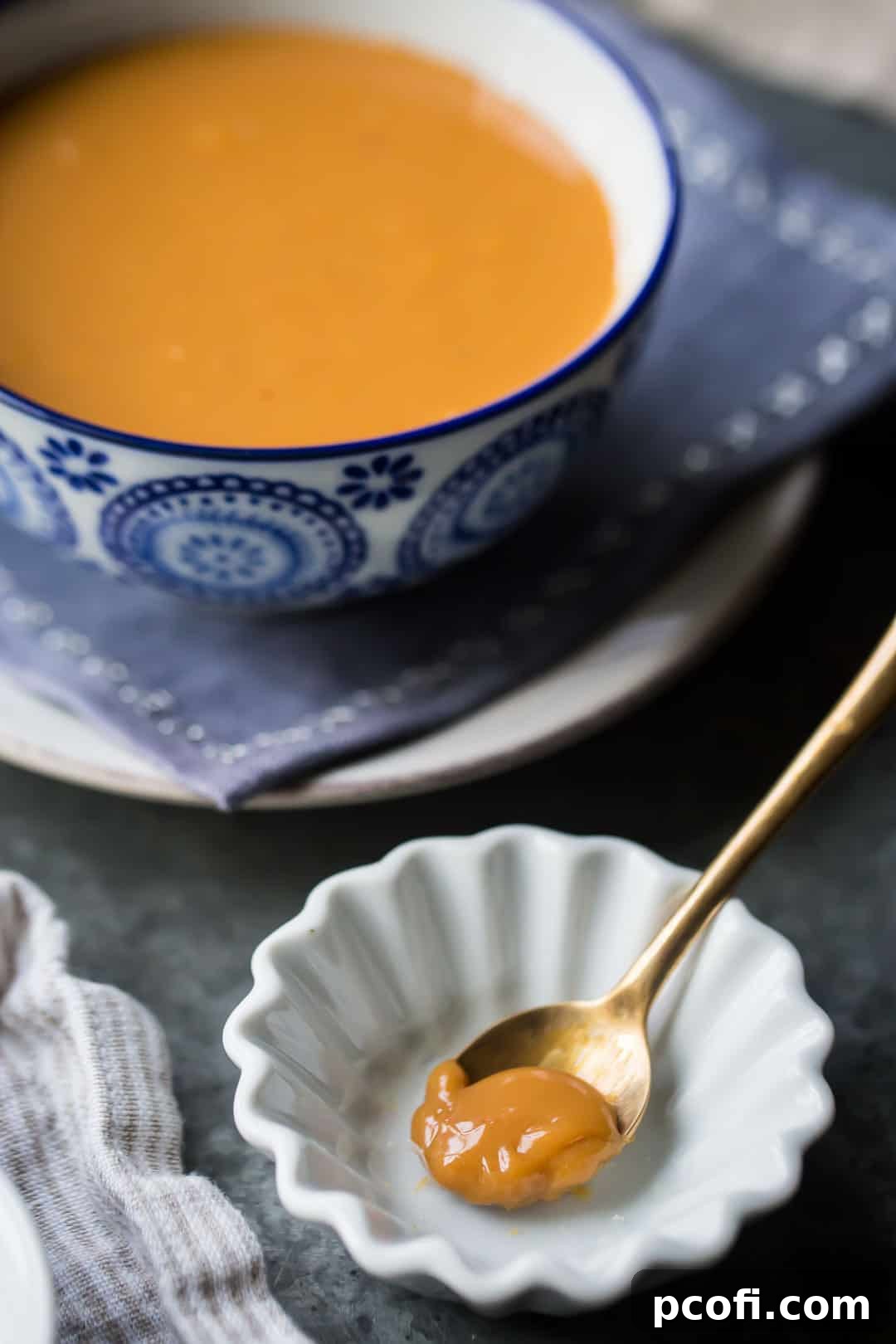 A spoonful of dulce de leche in a small white dish, with a larger bowl of dulce de leche in the background.