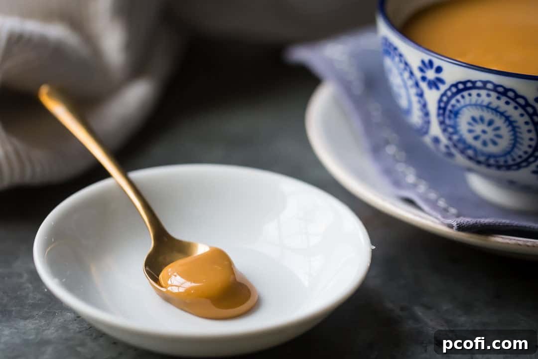 Gold spoonful of dulce de leche caramel on a white dish with a blue patterned bowl in the background.
