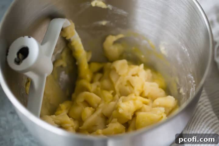 The choux pastry dough is vigorously beaten in a mixing bowl as eggs are incorporated, gradually transforming into a smooth, shiny, and stretchy batter perfect for making churros.