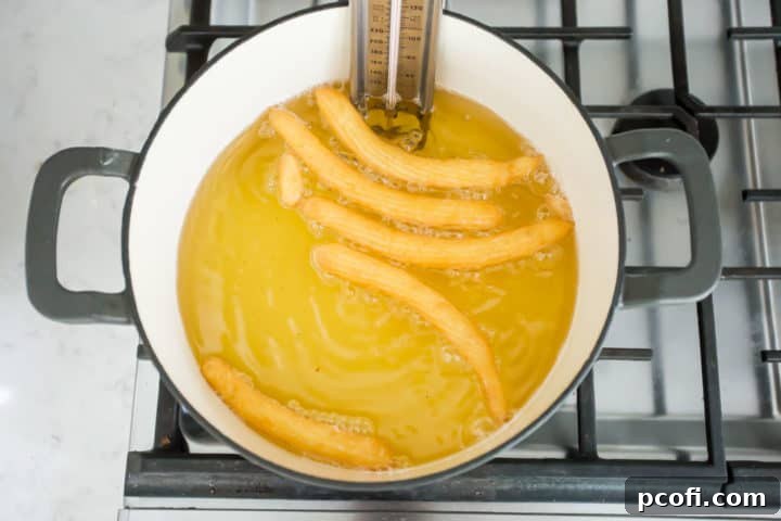 Several homemade churros are actively frying in bubbling hot oil within a Dutch oven, gradually turning golden brown and achieving their signature crispy texture.