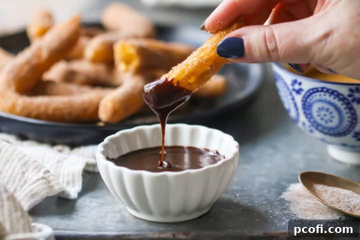 A freshly made churro is gracefully dipped into a rich, dark chocolate sauce, creating a tantalizing visual of the perfect sweet indulgence.