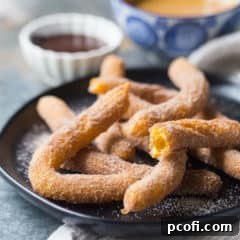 Homemade churros on a dark plate with chocolate sauce and dulce de leche in the background.