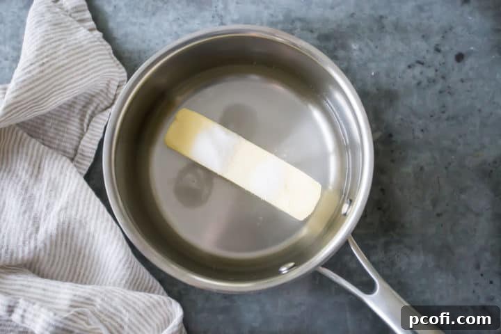 Water, butter, a hint of sugar, and salt are combined in a small saucepan over heat, illustrating the initial step in preparing the churro dough base.