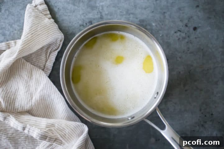 The mixture of water, butter, sugar, and salt comes to a gentle simmer in a small pot, indicating it's ready for the next step in creating the choux pastry for churros.