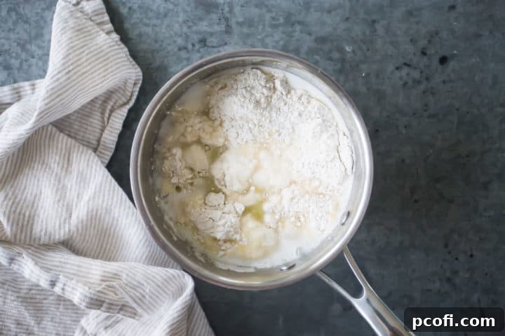 All-purpose flour is added suddenly and completely into the simmering liquid mixture in the small pot, forming the initial, seemingly chaotic stage of the choux pastry dough for churros.